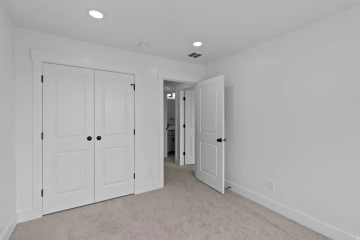 Plush carpet flooring, recessed ceiling lighting, white painted interior walls, white panel doors with black hardware, and white trim