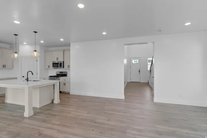 Open-concept living area featuring wood-finish flooring, recessed lighting, and a kitchen with an island, pendant lights, and stainless steel appliances