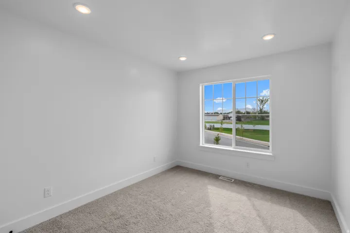Bright bedroom featuring expansive windows framing natural light, neutral wall finishes, recessed ceiling lighting, and soft carpet flooring overlooking landscaped grounds