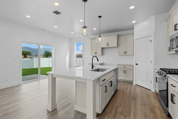 Modern kitchen featuring white cabinetry with brushed nickel hardware, a large waterfall-edge island with seating for multiple guests, stainless steel appliances including a gas cooktop and wall oven, pendant lighting with glass shades, and wood-finish fl