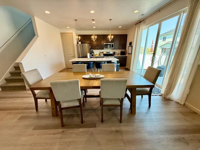 Open-concept living and dining area featuring wood-finish flooring, recessed ceiling lighting, and glass sliding doors with natural light