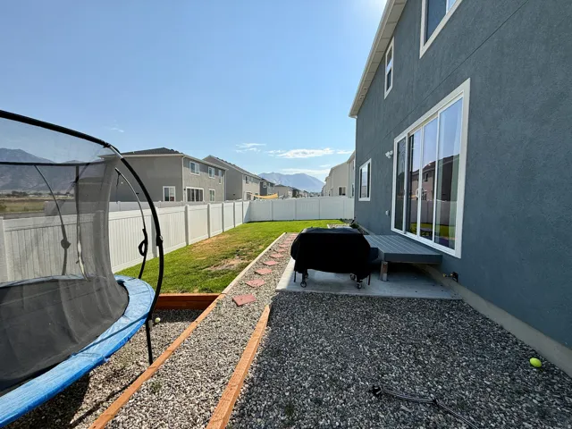 Spacious backyard featuring a manicured lawn, gravel hardscaping with brick edging, and a trampoline enclosure