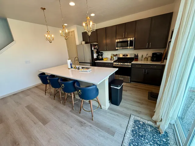 Spacious kitchen featuring a large central island with seating, dark wood-finish cabinetry, stainless steel appliances, and wood-finish flooring