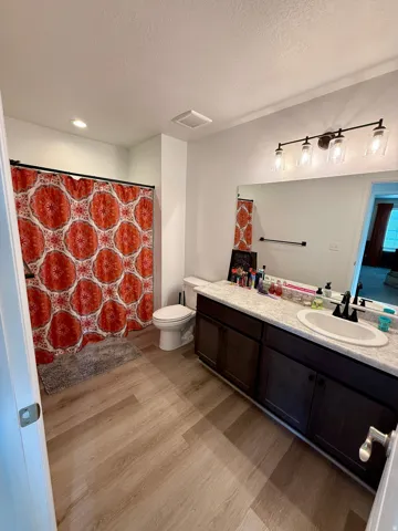 Bathroom featuring wood-finish flooring, a single vanity with dark wood-finish cabinetry, a white countertop, and a built-in mirror