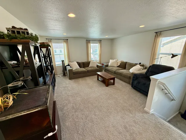 Spacious living area showcasing neutral carpet flooring, recessed ceiling lighting, and multiple windows with natural light