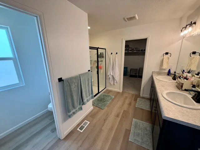Master Bath-Dual vanity with integrated sinks, wood-finish flooring, a glass-enclosed shower, and a separate water closet
