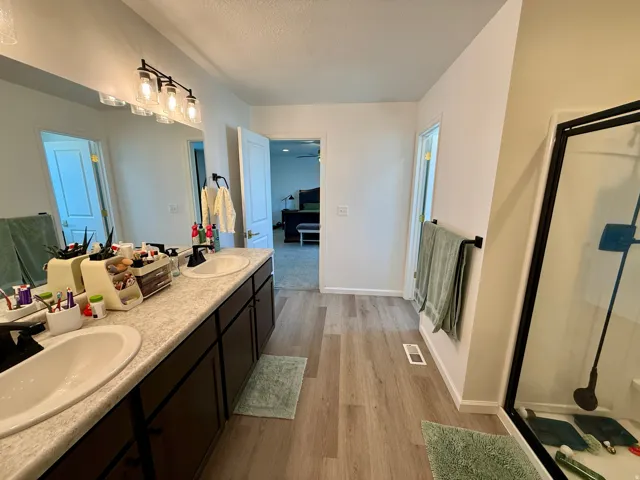 Master Bathroom featuring a dual vanity with undermount sinks, wood-finish flooring, a large wall mirror, and a shower enclosure with a black frame