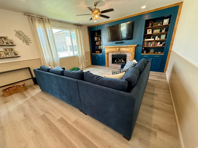 Spacious living room anchored by a custom built-in entertainment center with deep blue cabinetry, shelving, and a fireplace with metal surround