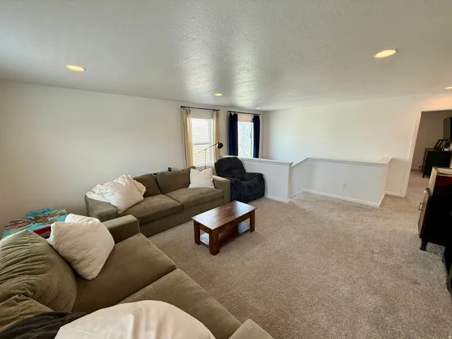 Spacious open-concept living area featuring neutral carpet flooring, recessed ceiling lighting, and multiple windows allowing natural light