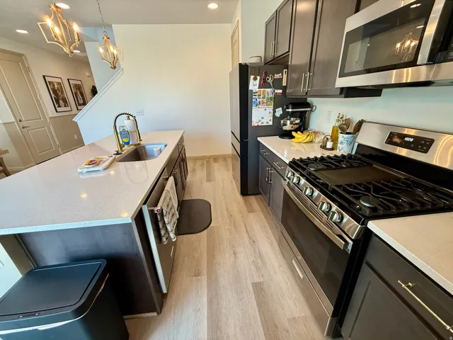 Kitchen featuring an island with an undermount sink, a gas range with an overhead microwave, wood-finish flooring, and dark cabinetry
