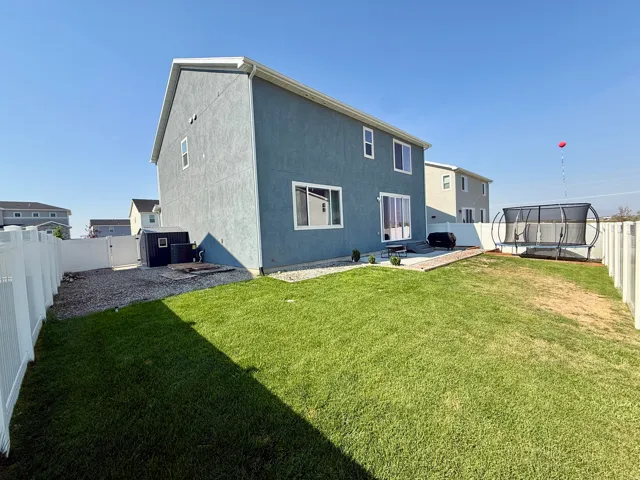 Expansive backyard with a manicured lawn, white privacy fencing, and a concrete patio area