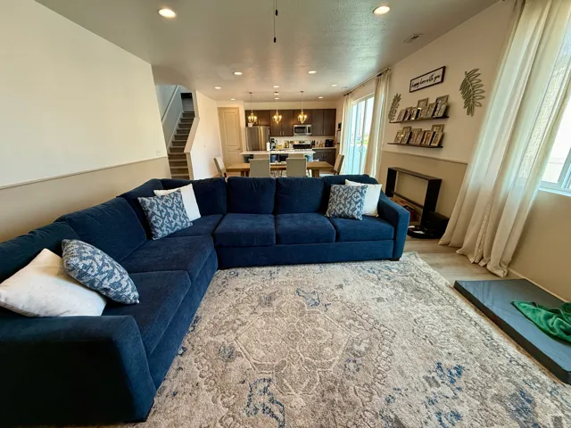 Spacious open-concept living area anchored by a generous L-shaped sectional arrangement, featuring neutral area rug, recessed ceiling lighting, and large windows with floor-to-ceiling drapery