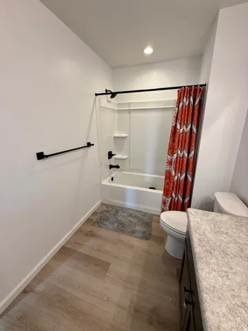 Tub/shower combination with black fixtures, wood-finish flooring, and vanity with stone-look countertop
