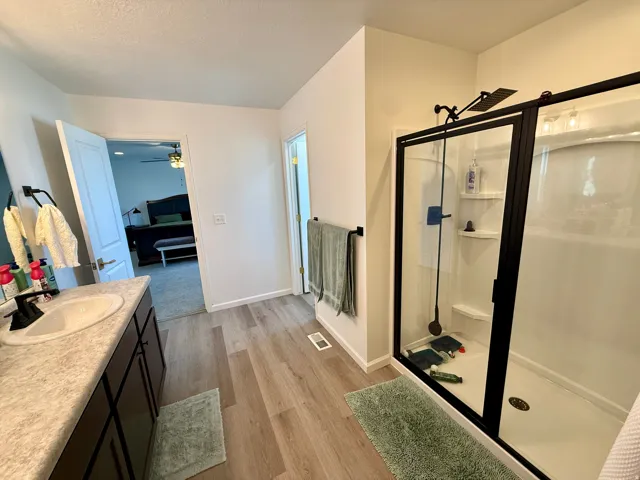 Master Bathroom- Spacious bathroom featuring a single vanity with an integrated sink, wood-finish flooring, and a walk-in shower with a black-framed glass enclosure