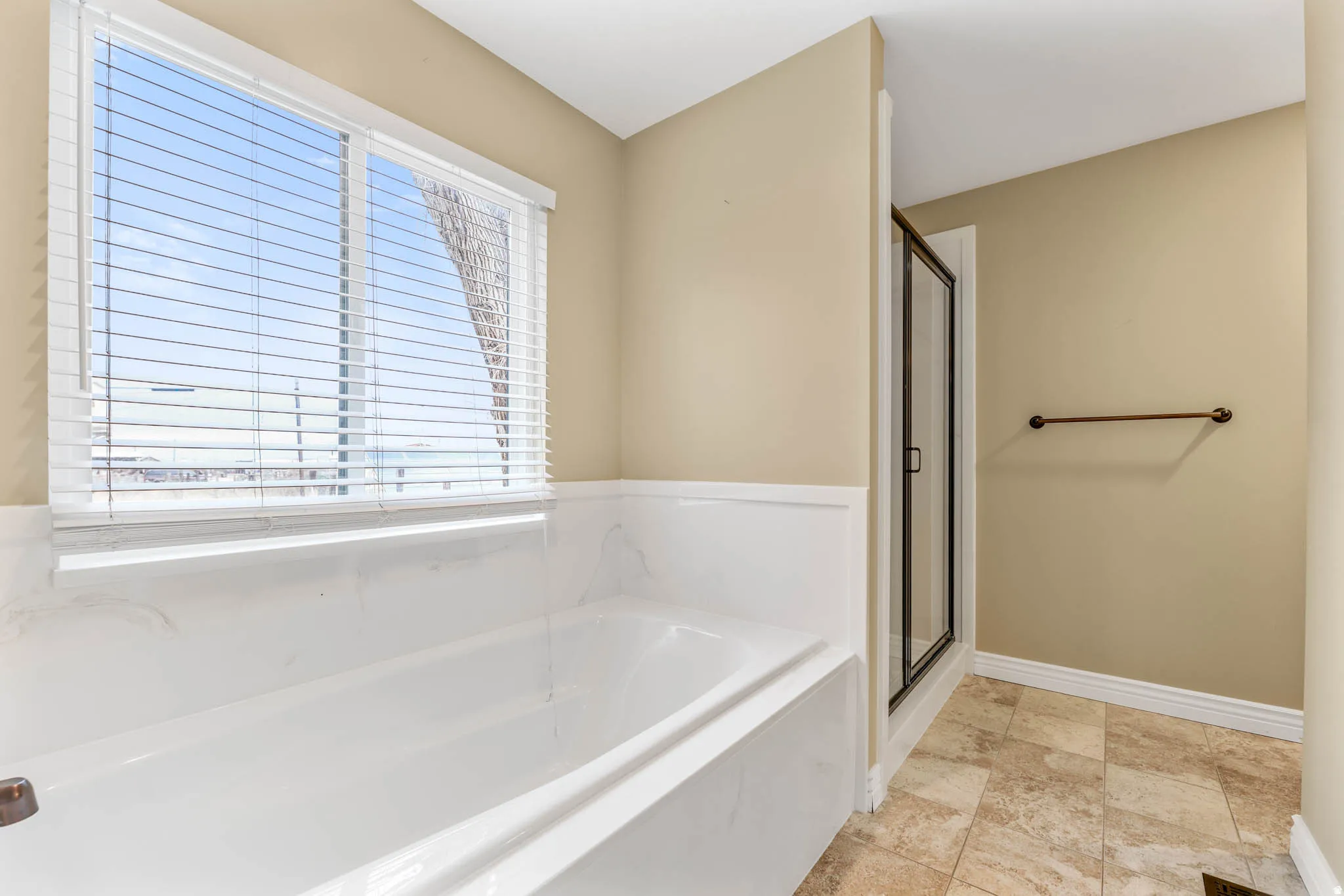 Soaking tub with a white tile surround, adjacent to a glass-enclosed shower with dark framing