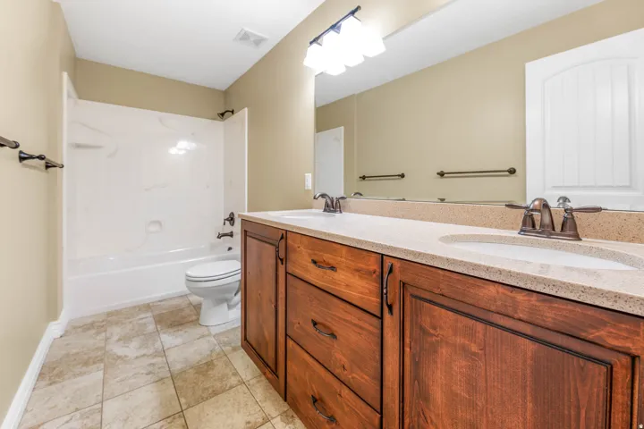 Dual vanity with integrated sinks, stone-finish countertop, wood-finish cabinetry, and tiled flooring