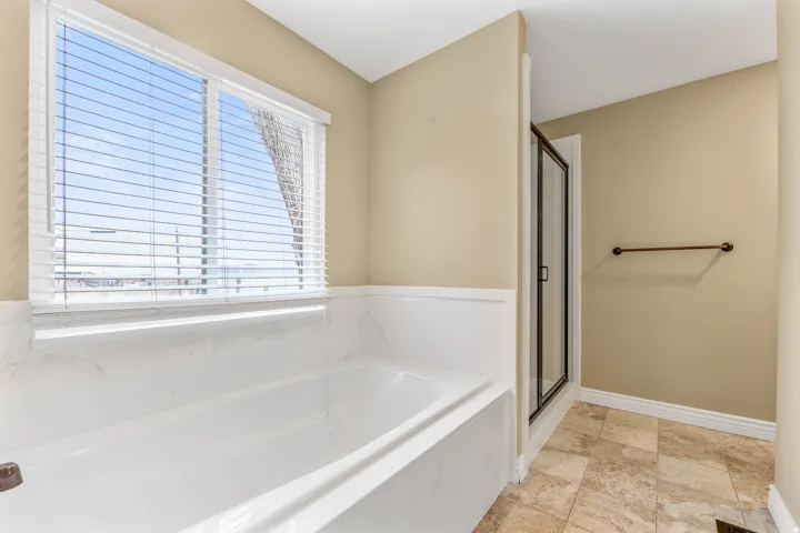 Soaking tub with a white tile surround, adjacent to a glass-enclosed shower with dark framing