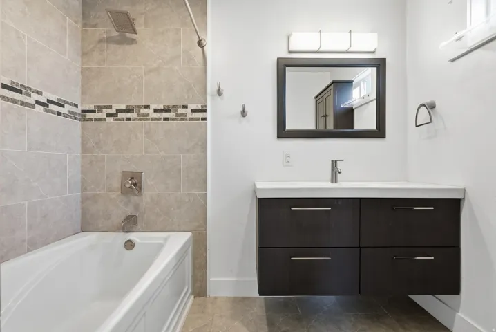 Full bathtub with tiled surround featuring a decorative mosaic accent