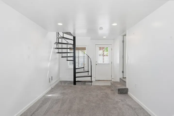 Spiral staircase with black metal railings, neutral carpeting, recessed ceiling lighting, and a window with blinds