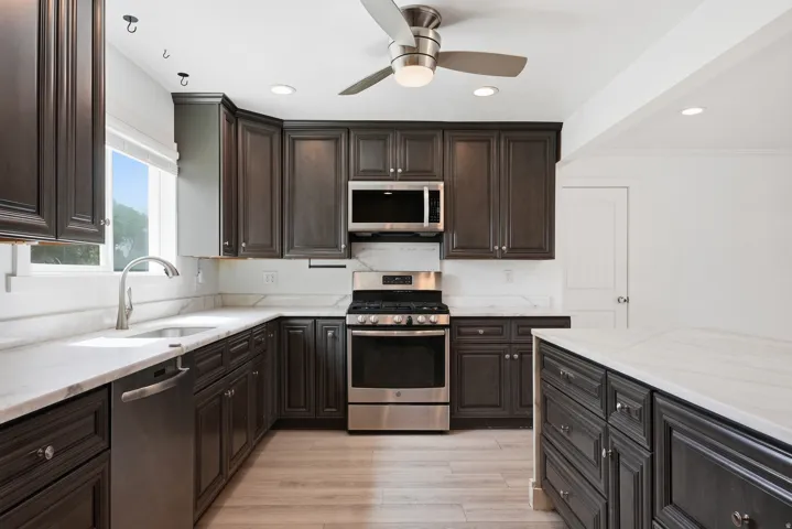 Kitchen featuring dark wood-finish cabinetry, light-toned countertops, stainless steel appliances, a ceiling fan with integrated lighting, and recessed lighting
