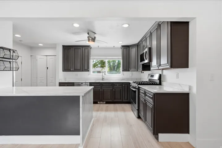Kitchen featuring dark wood cabinetry, light-toned wood-finish flooring, white countertops, stainless steel appliances, and recessed lighting
