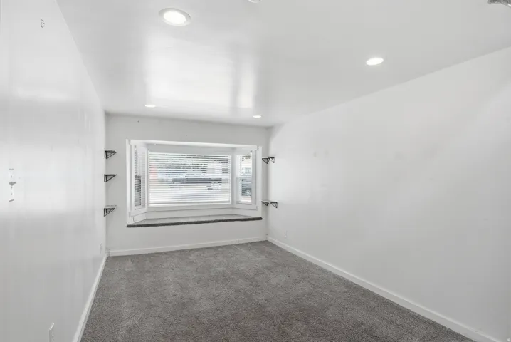Bay window with built-in seating, recessed lighting, wall-mounted shelving brackets, and carpet flooring