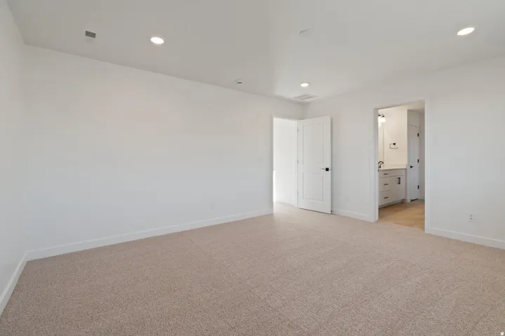 Light-colored carpeting with white walls, recessed ceiling lighting, and a white interior door with dark hardware