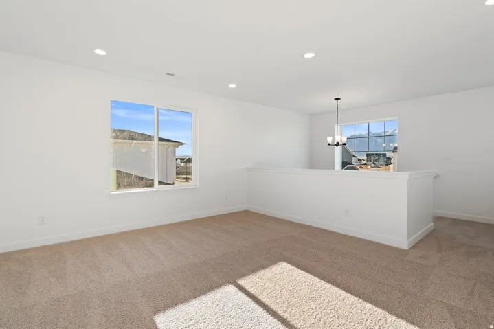 Recessed lighting, neutral carpet, white walls, white window trim, and a contemporary chandelier