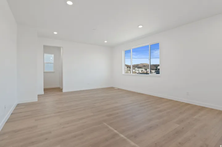 Expansive room featuring wood-finish flooring, recessed lighting, a large window, and white trim throughout