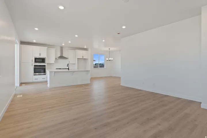 Open-concept layout featuring wood-finish flooring, white cabinetry, stainless steel appliances, and recessed lighting