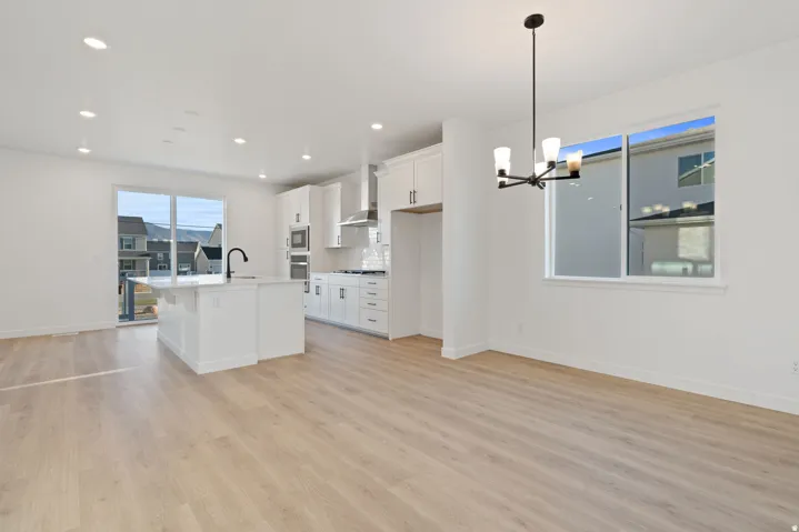 Modern kitchen featuring white cabinetry, a large center island with a sink, stainless steel appliances, and light wood-finish flooring
