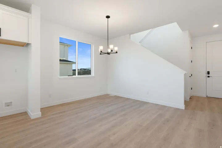 Light wood-finish flooring, white walls, and a contemporary black chandelier complement the bright window