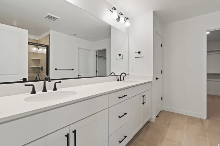 Primary bathroom featuring a dual-sink vanity with white cabinetry, quartz countertop, and matte black hardware and faucets