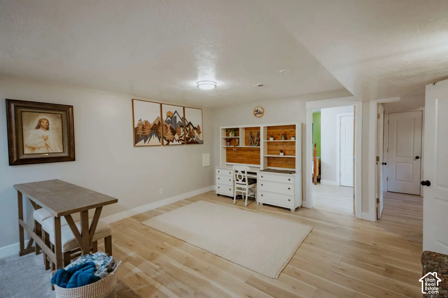 Light-toned wood-finish flooring, white walls, and built-in white desk cabinetry featuring natural wood shelving accents