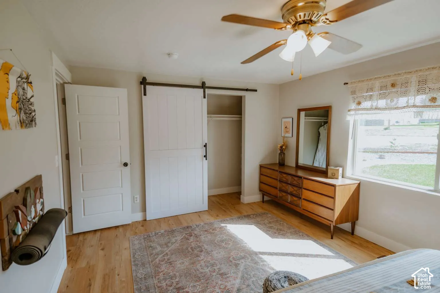 Wood-finish flooring, white sliding barn door on a black metal track, five-panel interior door, and a ceiling fan with integrated lighting