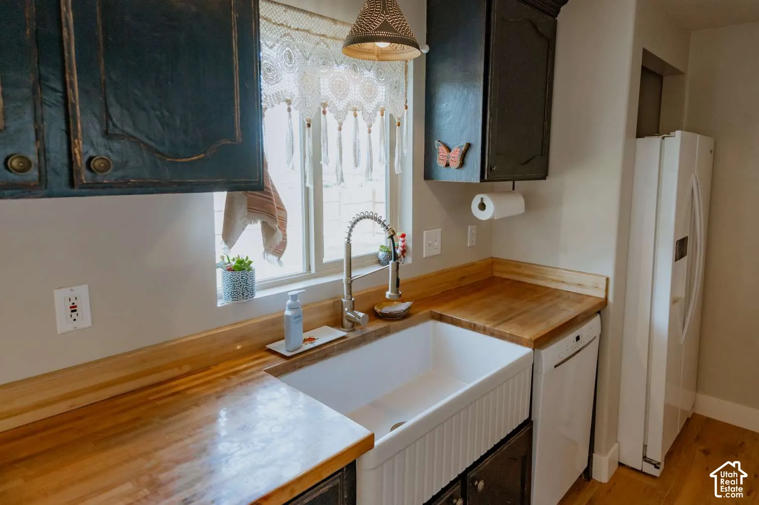 Kitchen area featuring butcher block countertops, a white farmhouse-style sink, a high-arc pull-down faucet, and dark-finish cabinetry