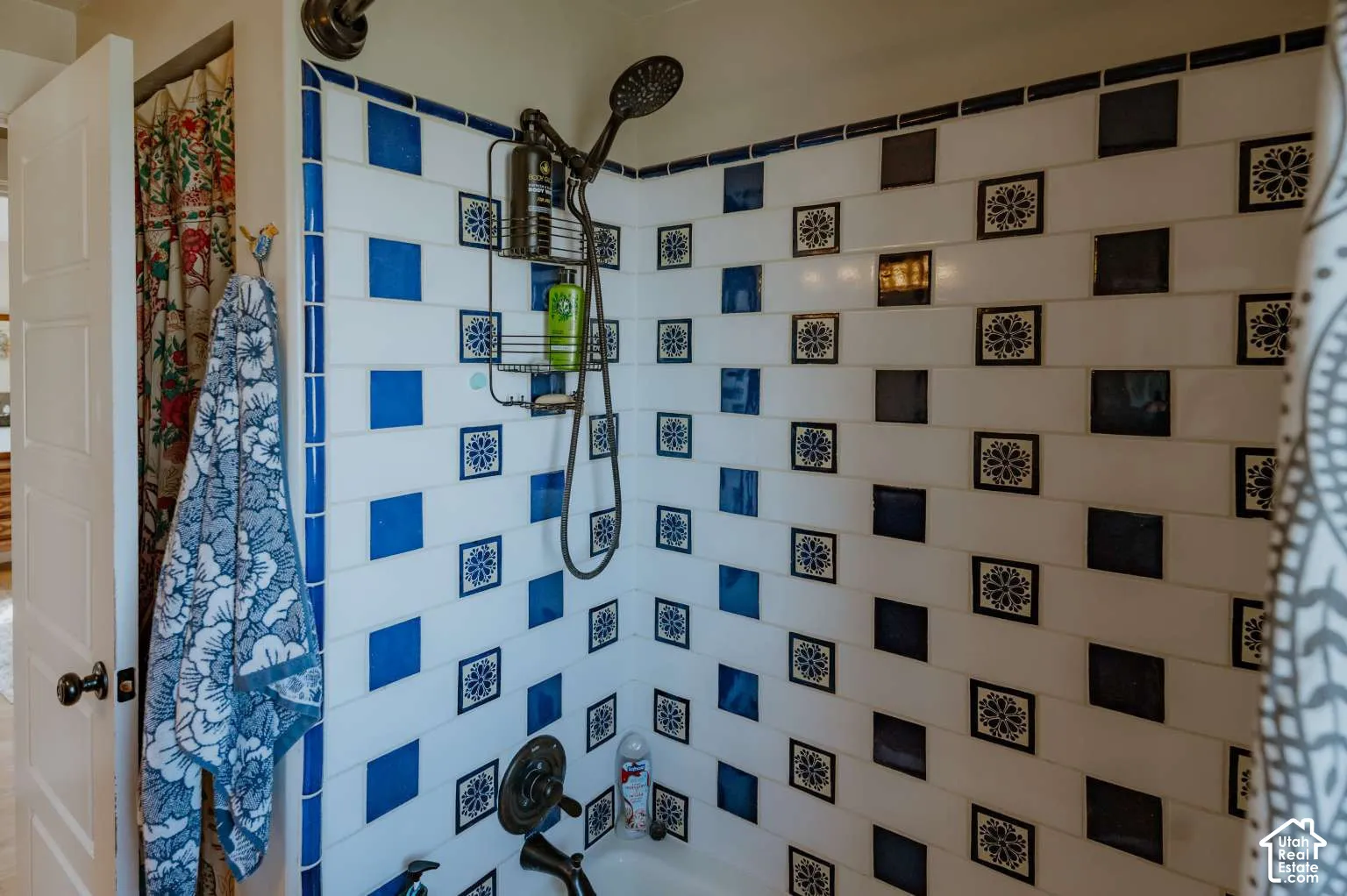Shower area featuring a white subway tile surround with decorative blue square accent tiles and a bronze-finish handheld shower fixture