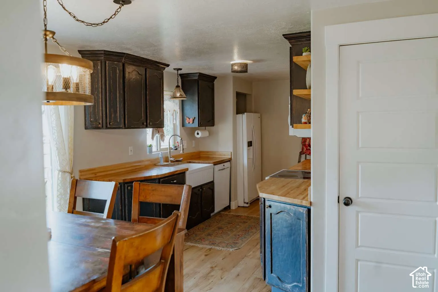 Kitchen featuring dark cabinetry, wood countertops, a white apron-front sink, open shelving, and wood-finish flooring