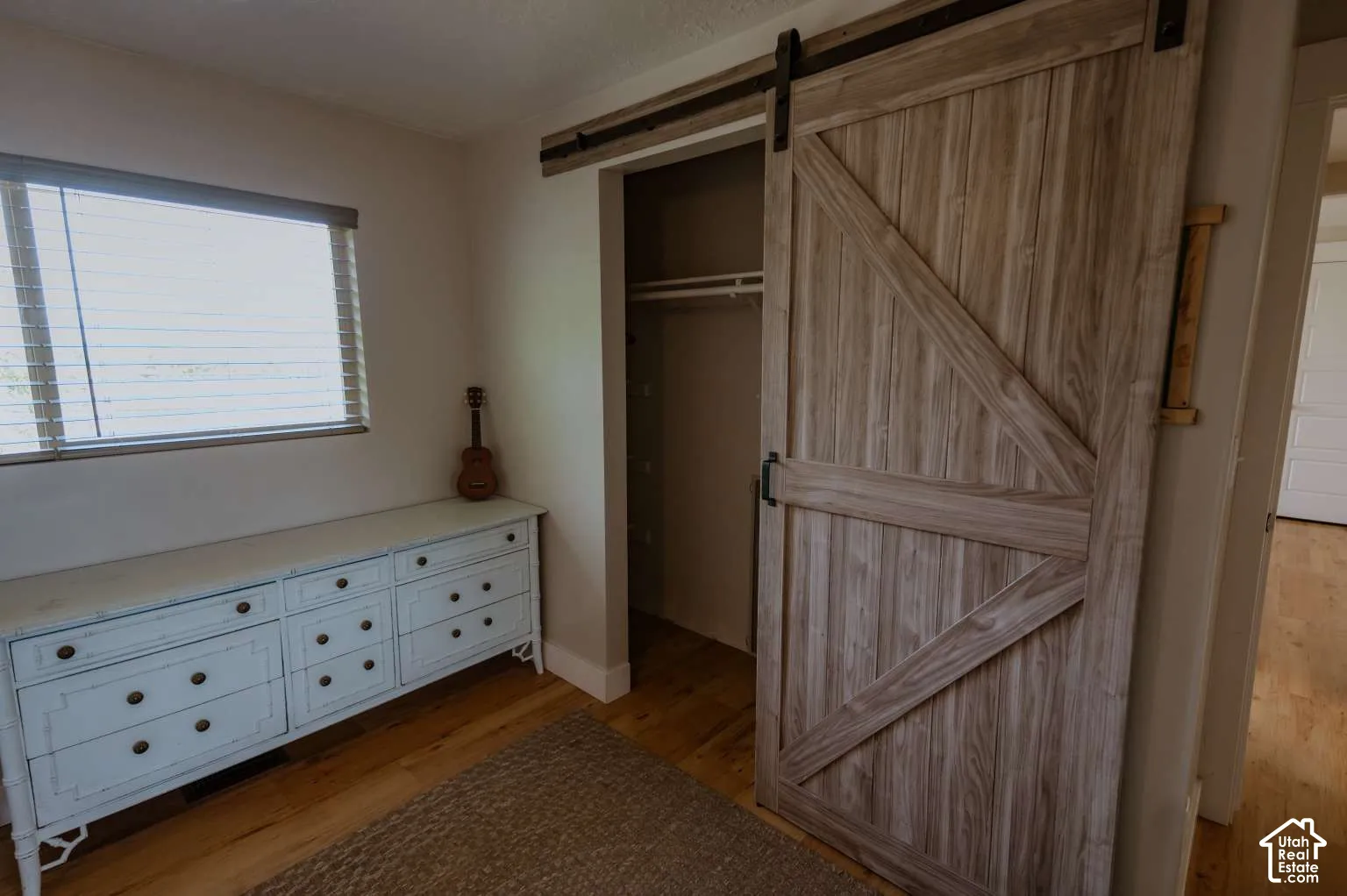 Interior featuring a sliding wood-finish barn door with a matte black track system, horizontal window blinds, and wood-finish flooring