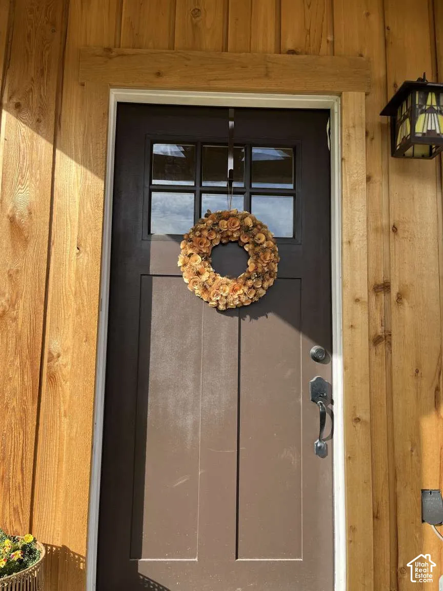 Entry door featuring a multi-pane glass window insert, dark-finish hardware, vertical wood siding, and an attached decorative glass wall lantern