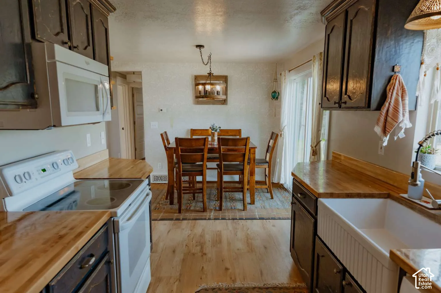 Kitchen featuring dark cabinetry, wood-surface countertops, a white farmhouse-style apron sink, and wood-finish flooring