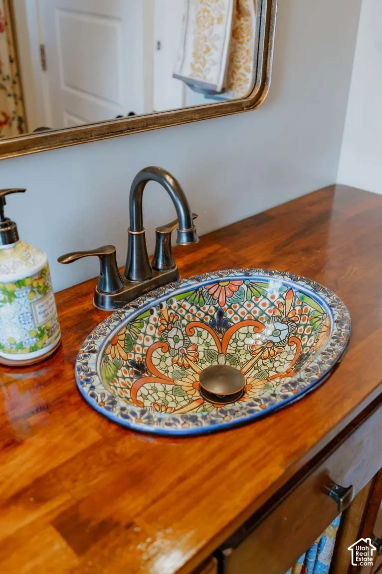 Vanity featuring a wood-surface countertop, an oval drop-in sink with decorative hand-painted detailing, a high-arc bronze-tone faucet, and a wall-mounted mirror