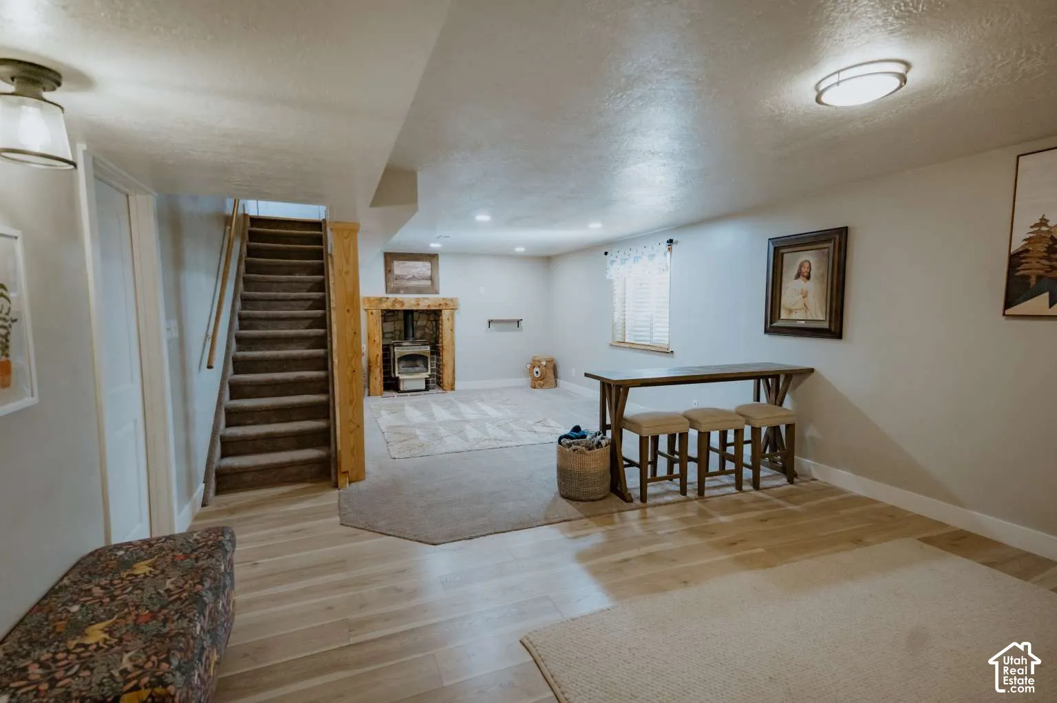 Interior space featuring wood-finish flooring, a stone-surround fireplace with a timber mantel, recessed lighting, and carpeted stairs with a wood railing