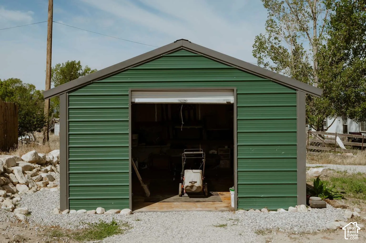 Detached metal storage structure featuring corrugated green siding, a roll-up garage door, and a gravel perimeter base