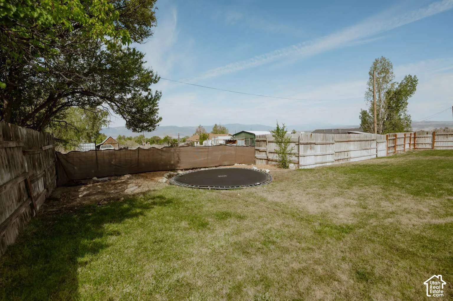 Backyard featuring a grass lawn, wood fencing, and mature trees with mountain scenery