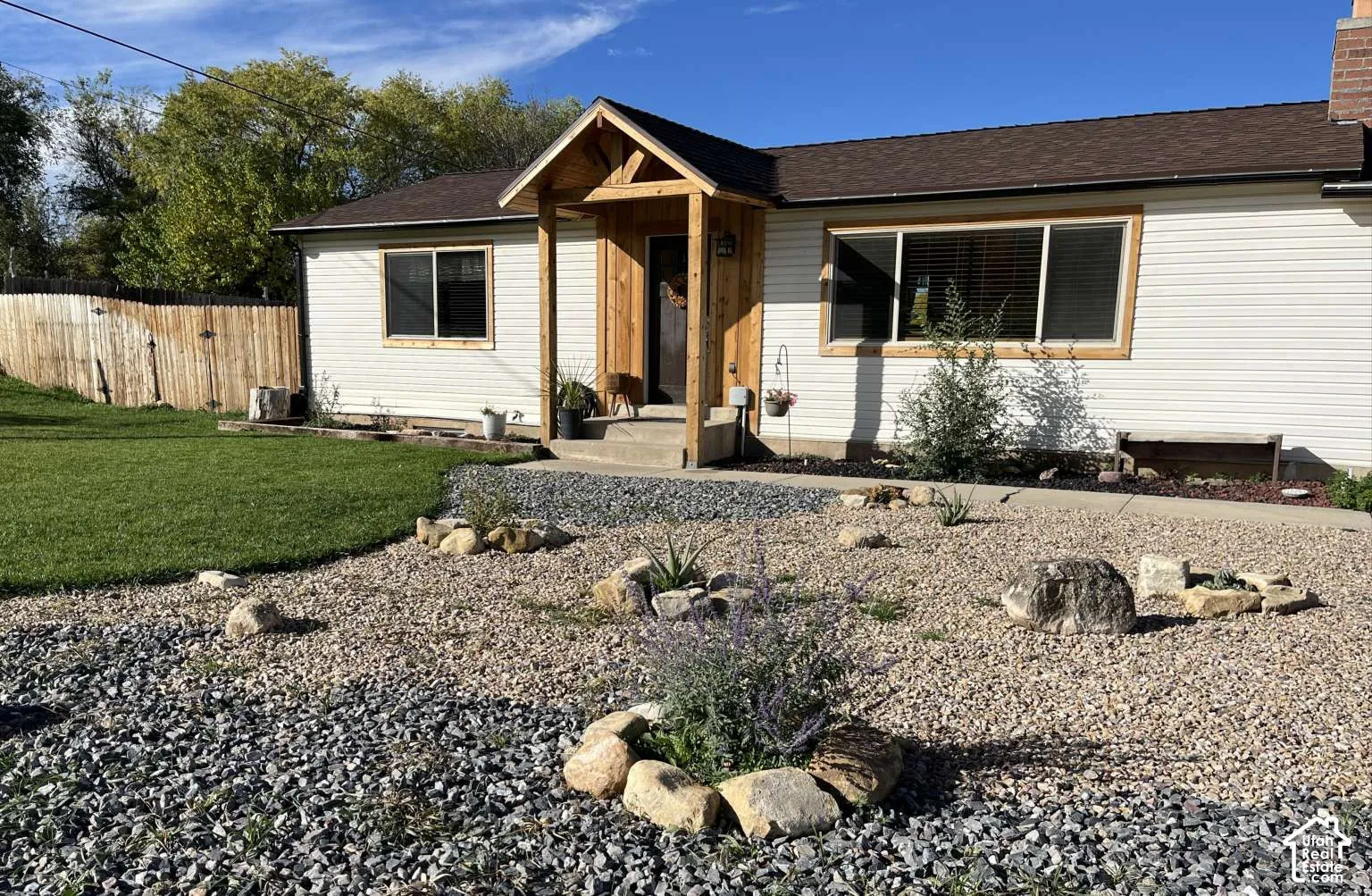 Exterior featuring light-colored horizontal siding, a timber-framed entryway porch, xeriscaped front yard with decorative stone, and a wood-slat perimeter fence