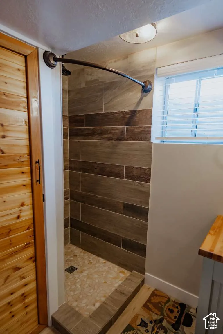 Walk-in shower featuring horizontal wood-finish wall tile, pebble-style floor tile, a curved shower rod, and a natural wood-paneled door