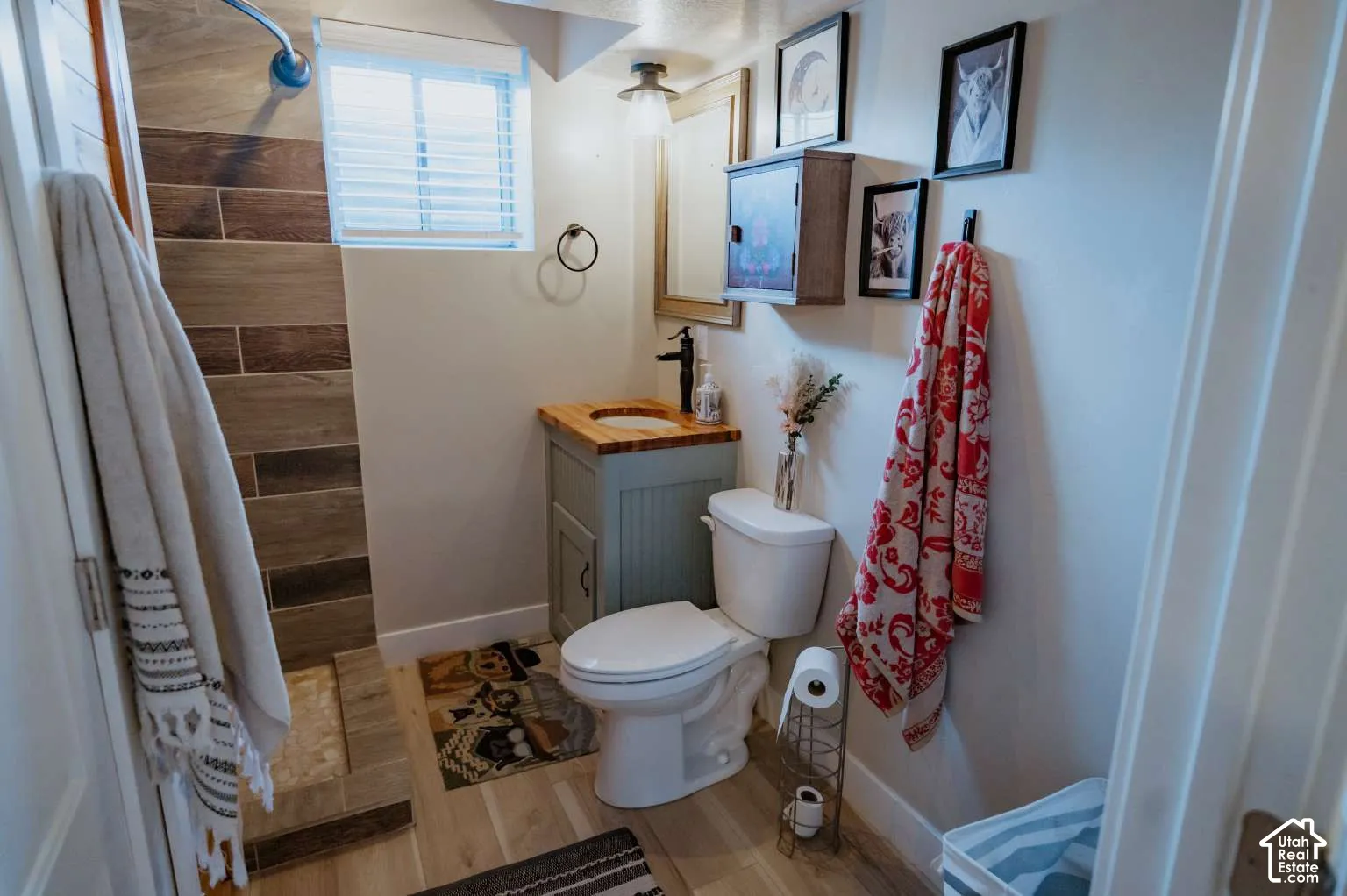 Bathroom featuring a walk-in shower with horizontal tile surround, wood-finish flooring, vanity with a wood countertop, and matte black plumbing fixtures