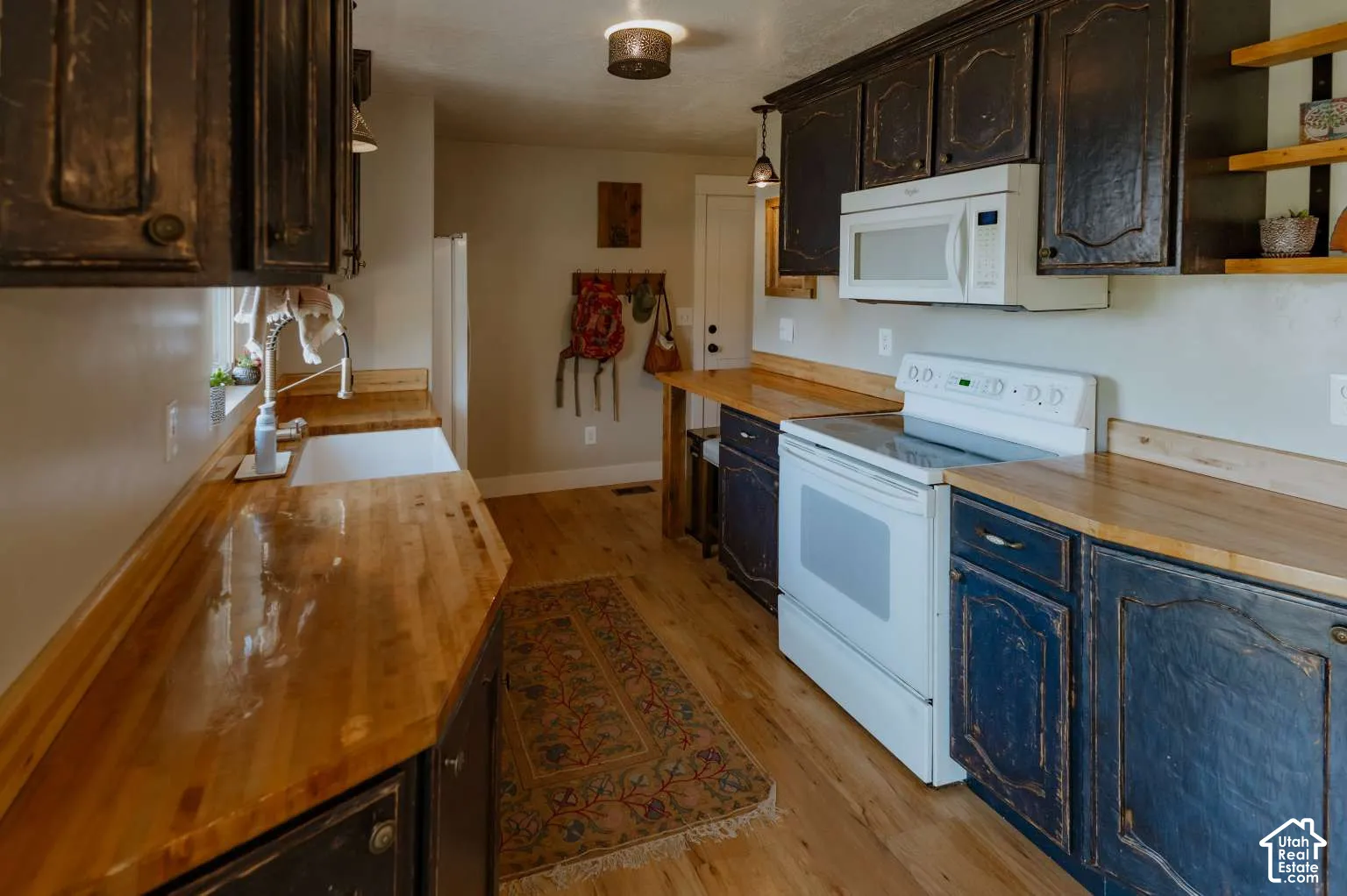 Kitchen featuring dark-finished cabinetry, wood countertops, a white farmhouse-style sink, built-in light-colored appliances, and wood-finish flooring