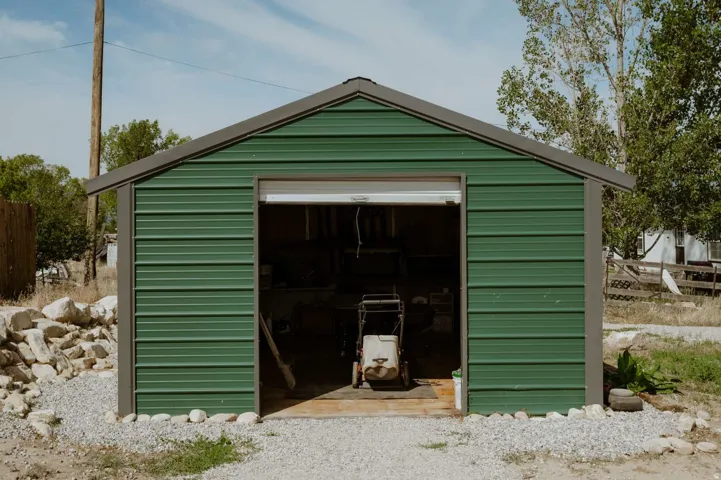 Detached shed with green corrugated metal siding, a gray sloped roof, and a partial roll-up door